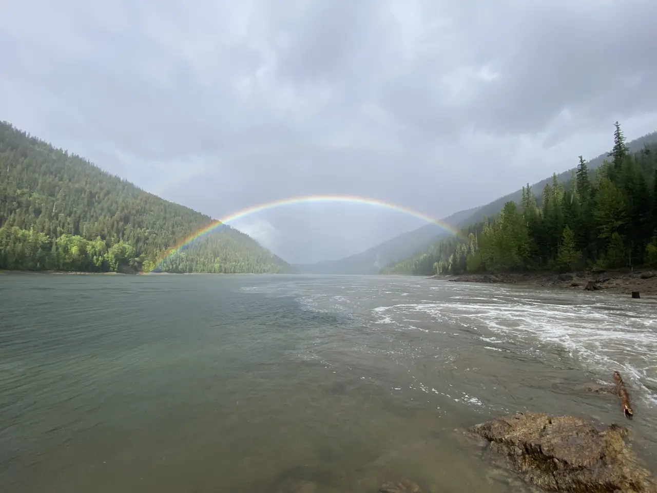 Rainbow over a lake framed by forested mountains