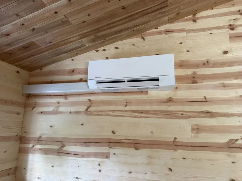 Finished wall-mounted mini split indoor head on a wood wall, with the line-set cover in place