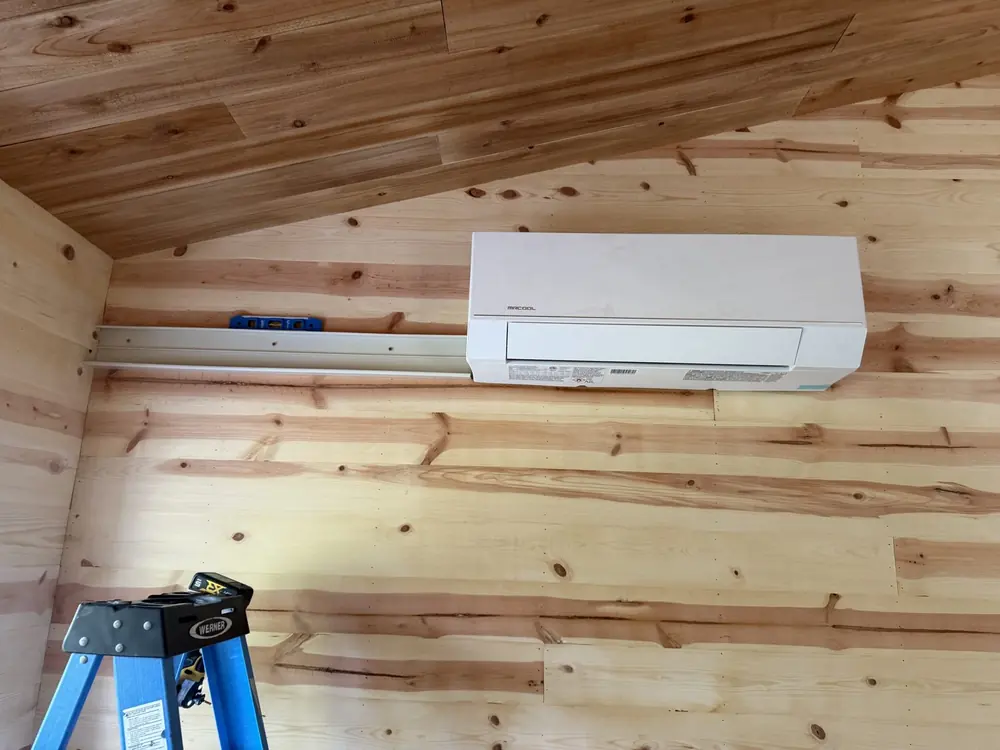Wall-mounted mini split indoor head on a wood wall, line-set cover beside it