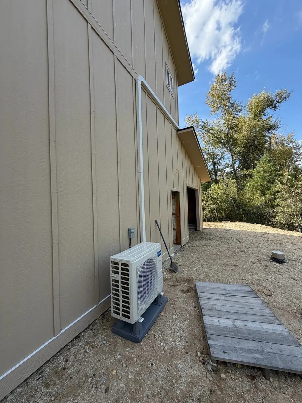 Mini split outdoor condenser on a pad against the siding, line-set cover running up the wall