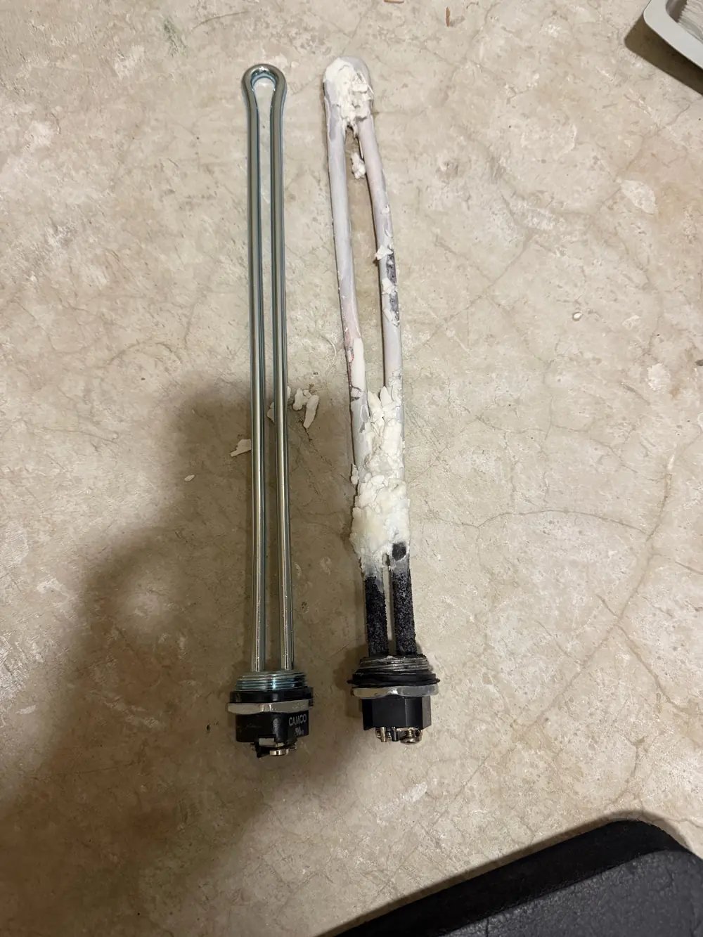 A clean electric water heater element next to a heavily scaled one