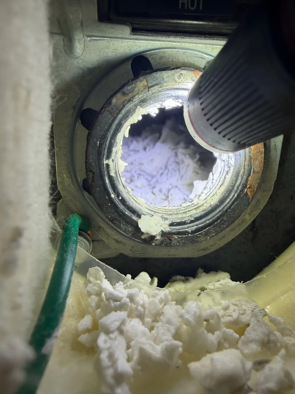 Scale buildup inside an electric water heater element port with a vacuum nozzle beside it